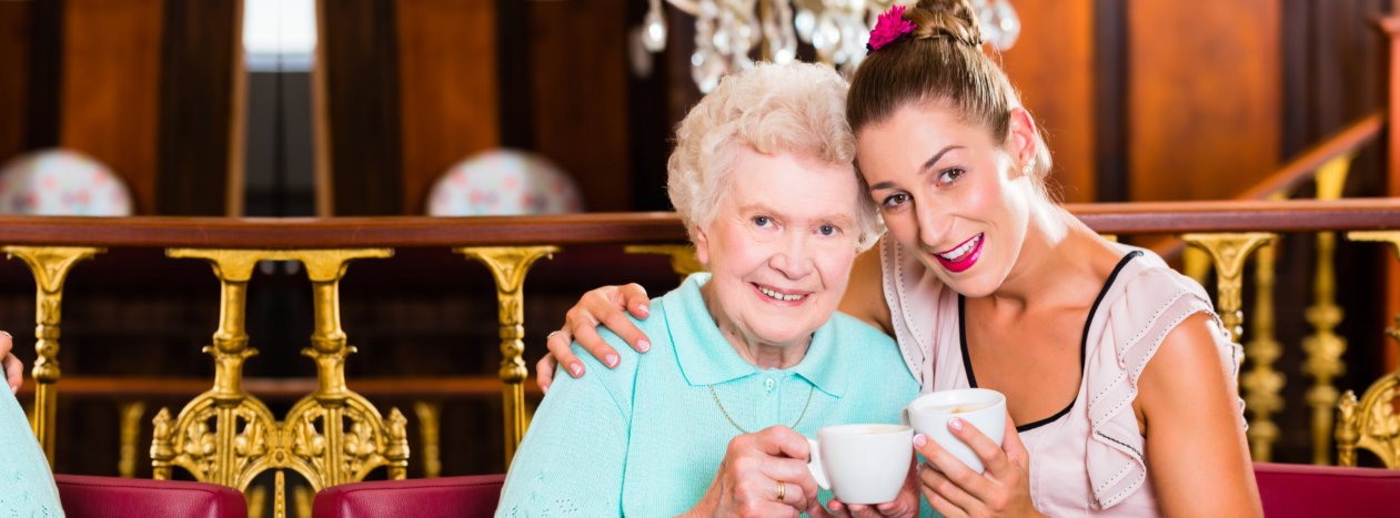 Old woman is drinking tea with her caregiver